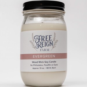 Pu&ograve; includere: Una candela in vetro bianco in un barattolo con un coperchio nero. L'etichetta recita "FREE REIGN FARM EVERGREEN Wood Wick Soy Candle No Phthalates, Paraffin or Dyes Approx: 13 oz. | 80 Hr. Burn"