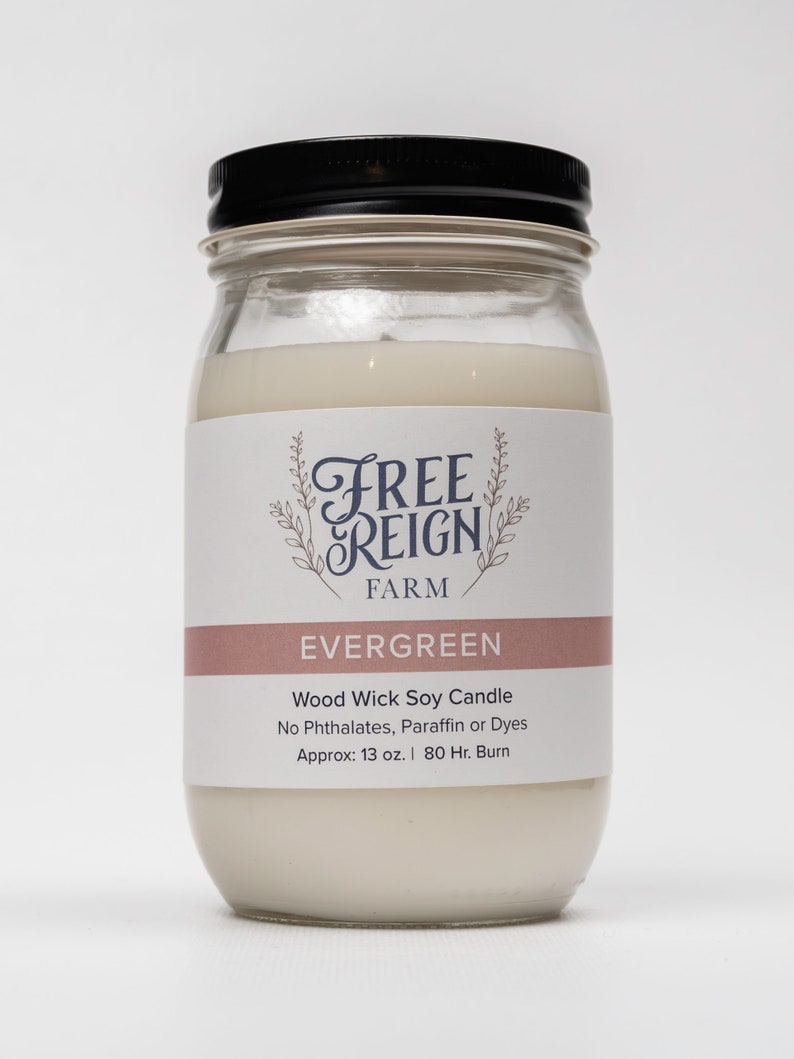 Pu&ograve; includere: Una candela in vetro bianco in un barattolo con un coperchio nero. L'etichetta recita "FREE REIGN FARM EVERGREEN Wood Wick Soy Candle No Phthalates, Paraffin or Dyes Approx: 13 oz. | 80 Hr. Burn"