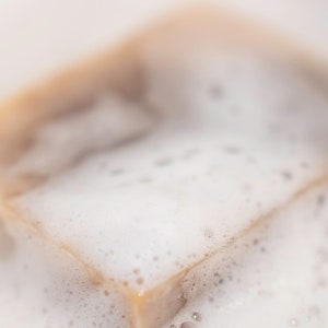 May include: A close-up of a bar of soap with a light brown color, covered in white foam.