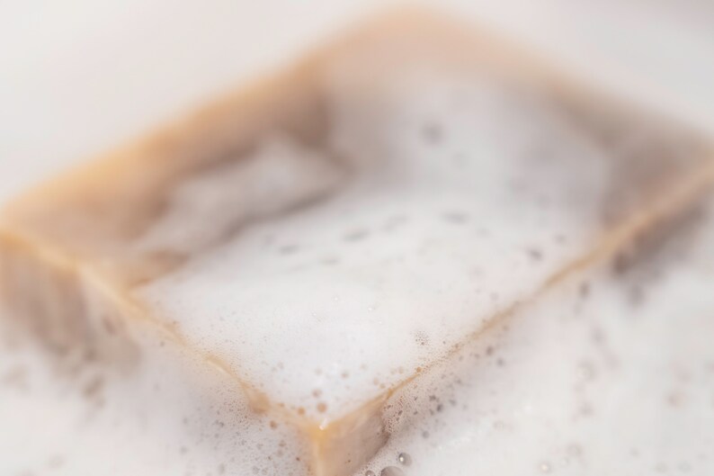 May include: A close-up of a bar of soap with a light brown color, covered in white foam.