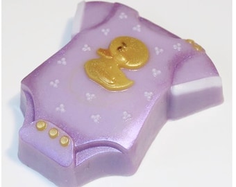 May include: A purple baby onesie soap with a gold duck design and gold buttons. The soap is decorated with small white dots.