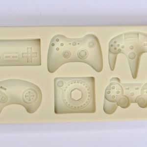 May include: A silicone mold for making cake decorations shaped like different video game controllers. The mold includes a Nintendo, Sega Genesis, Playstation, N64, and Xbox controller.