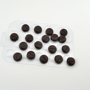 May include: A clear plastic pill tray with dark brown chocolate pills in most of the compartments.