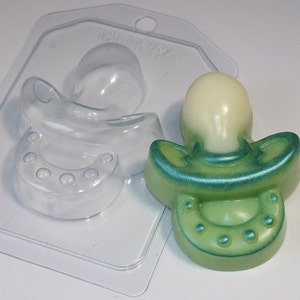 May include: A clear plastic mold for making a baby pacifier shaped soap. The mold is shown with a green and white soap that has been made in the mold.