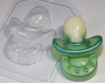 May include: A clear plastic mould for making a baby pacifier shaped soap. The mould is shown with a green and white soap that has been made in the mould.