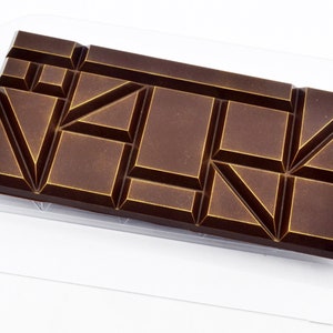 May include: A dark brown chocolate bar with a geometric pattern of gold lines. The bar is in a clear plastic wrapper.