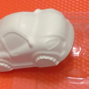 May include: White plastic mold of a car, with detailed wheels and a smooth surface. The mold is designed for making crafts or decorations.