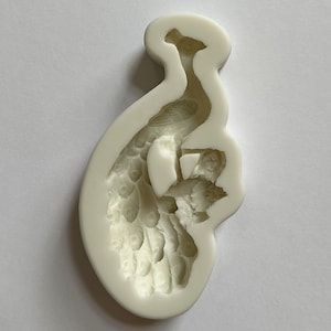 Peut inclure: Moule en silicone blanc en forme de paon avec ses plumes de queue déployées. Le moule est conçu pour réaliser des décorations de gâteaux ou d'autres créations comestibles.