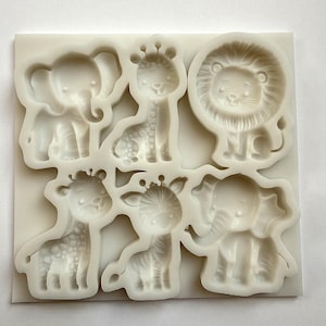 Könnte beinhalten: Eine weiße Silikonform mit sechs Tierformen: ein Elefant, zwei Giraffen, ein Löwe und ein Zebra. Die Form ist mit detaillierten Tiermerkmalen gestaltet, perfekt für Bastelprojekte. Die Tiere sind im Cartoon-Stil.