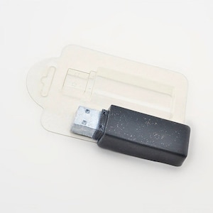 Könnte beinhalten: Ein schwarzer USB-Stick mit einem silbernen USB-Stecker. Der Stick befindet sich in einer transparenten Plastikverpackung mit einer Aufhängeschlaufe.