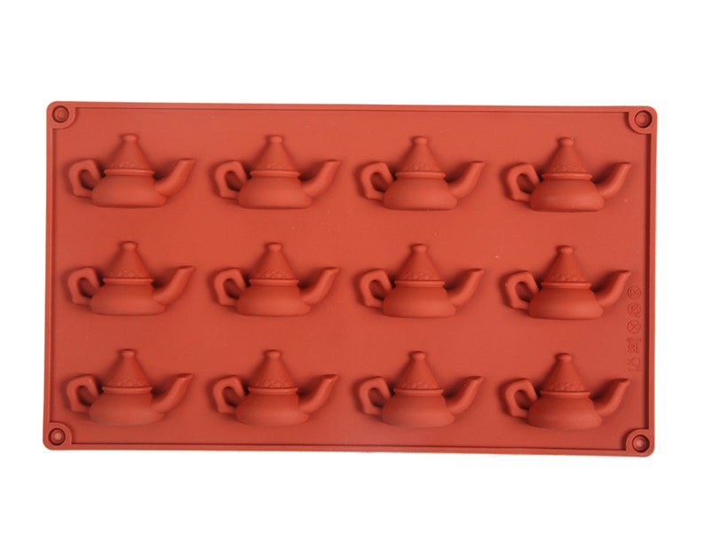 May include: A red silicone mold with 12 teapot-shaped cavities. The mold is designed for making small, decorative teapots.