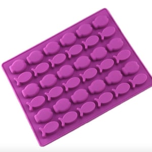 Puede incluir: Molde de silicona morado con 24 cavidades en forma de pez. El molde está diseñado para hacer chocolate, caramelos o hielo.