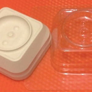 May include: Two square plastic molds for making candles. One mold is white and the other is clear.