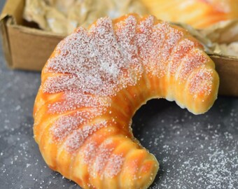 May include: A crescent-shaped pastry dusted with sugar. The pastry is golden brown and has a flaky texture.