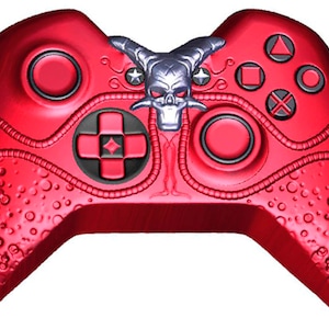 May include: A red Xbox controller with a skull design on the front. The controller has a textured surface and a black and red color scheme.