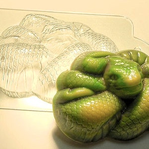 Puede incluir: Un molde de silicona en forma de serpiente verde y amarillo para hacer jabón u otras manualidades. El molde tiene la forma de una serpiente enroscada con la cabeza apoyada en su cuerpo.