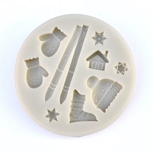 Könnte beinhalten: Silikonform mit winterlichen Designs, darunter Fäustlinge, Skier, ein Haus, eine Schneeflocke, ein Stiefel und eine Mütze.