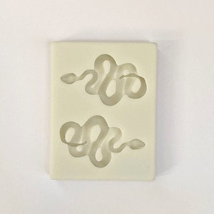 Puede incluir: Un molde de silicona blanco con dos diseños de serpientes. Las serpientes están enroscadas en forma de círculo.