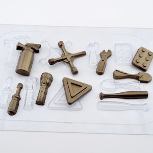 Könnte beinhalten: Eine transparente Kunststoffschale enthält verschiedene Werkzeugobjekte in Gold und klarem Kunststoff. Zu den Werkzeugen gehören ein Schraubenschlüssel, ein Schraubendreher, eine Taschenlampe und ein Baseballschläger. Die Schale befindet sich auf einer weißen Oberfläche.