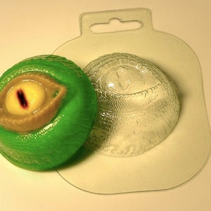 Puede incluir: Un molde de plástico verde para hacer un globo ocular gigante con una pupila roja. El molde está en dos piezas, una para el globo ocular y otra para la piel circundante.