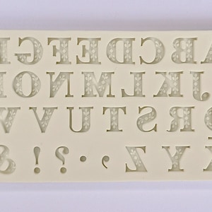Puede incluir: Molde de silicona blanco con letras de la A a la Z y signos de puntuación. Las letras tienen un patrón decorativo.