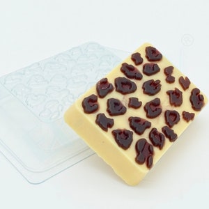 May include: A clear plastic mold with a white chocolate bar with a leopard print design. The chocolate bar is filled with dark brown chocolate.