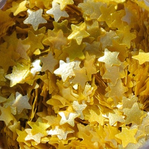 Könnte beinhalten: Ein Nahaufnahmebild eines Behälters, der mit goldenen Glitzersternen gefüllt ist. Die Sterne sind zufällig verteilt und alle gleich groß und gleich geformt.