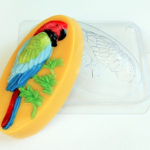 May include: A yellow soap bar with a parrot design. The parrot is blue, green, and red with a black head. The soap is in a clear plastic mold.