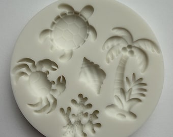 May include: A white silicone mold featuring raised designs of a turtle, crab, seashell, palm tree, and coral. The circular mold is designed for creating decorative elements for crafts or baking projects.