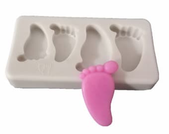 May include: A white silicone mold with four baby foot shapes. A pink baby foot is sitting next to the mold.