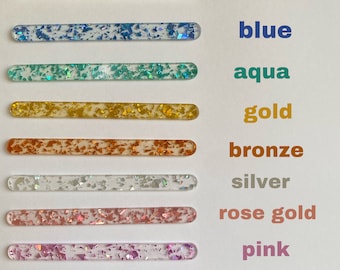 May include: Nine clear acrylic sticks with different coloured glitter embedded inside. The sticks are arranged vertically from top to bottom with the following colours: green, blue, aqua, gold, bronze, silver, rose gold, pink, and purple. The colours are labelled on the right side of the image.