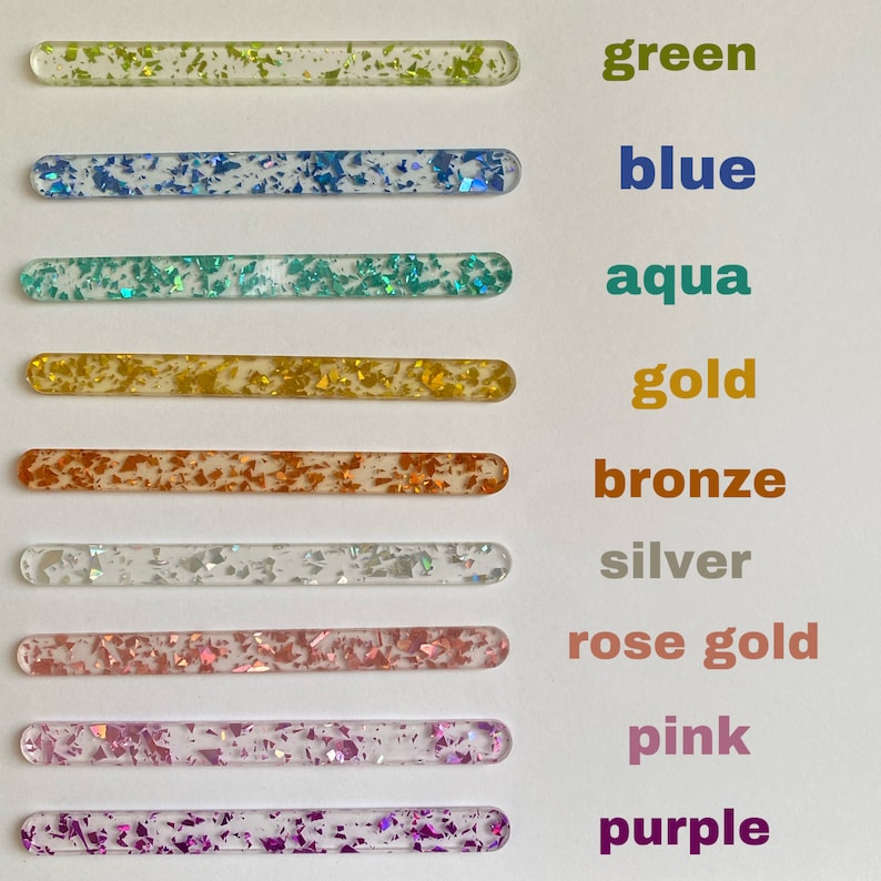Peut inclure: Neuf b&acirc;tonnets en acrylique transparent avec des paillettes de diff&eacute;rentes couleurs incrust&eacute;es &agrave; l'int&eacute;rieur. Les b&acirc;tonnets sont dispos&eacute;s verticalement de haut en bas avec les couleurs suivantes&nbsp;: vert, bleu, aqua, or, bronze, argent, or rose, rose et violet. Les couleurs sont &eacute;tiquet&eacute;es sur le c&ocirc;t&eacute; droit de l'image.