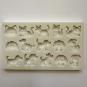 May include: An off-white silicone mould with a rectangular shape, featuring cat and dog designs. The mould includes detailed impressions of cat faces, cats in different poses, and several dog breeds. The design is suitable for creating decorative items.