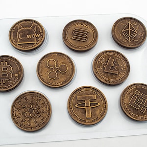 May include: A set of nine gold-colored metal coins featuring various cryptocurrency logos, including Bitcoin, Ethereum, Litecoin, and Solana. The coins are arranged on a clear plastic tray.