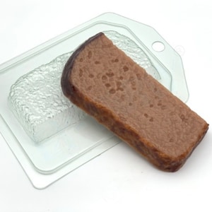 Puede incluir: Un molde de plástico transparente para hacer un pan. El molde se muestra con un objeto con forma de pan marrón en su interior.