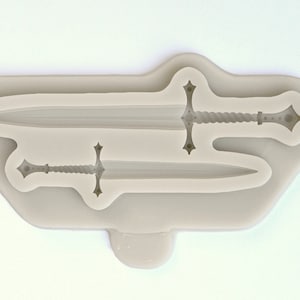 May include: A silicone mold for making two swords, one with a twisted handle and one with a straight handle. The mold is light gray and has a smooth surface.