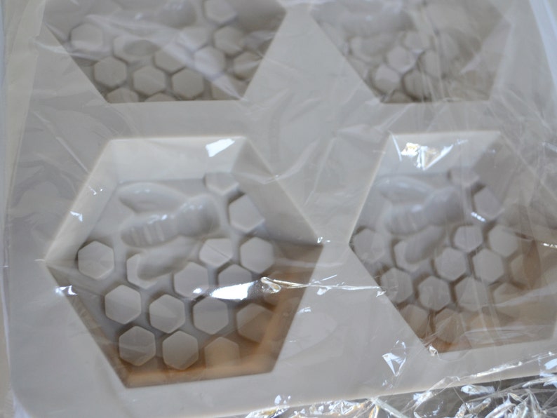 May include: A white silicone mould for crafting soaps or other items. The mould has a honeycomb design with a bee in each hexagonal cavity. The mould is packaged in clear plastic.