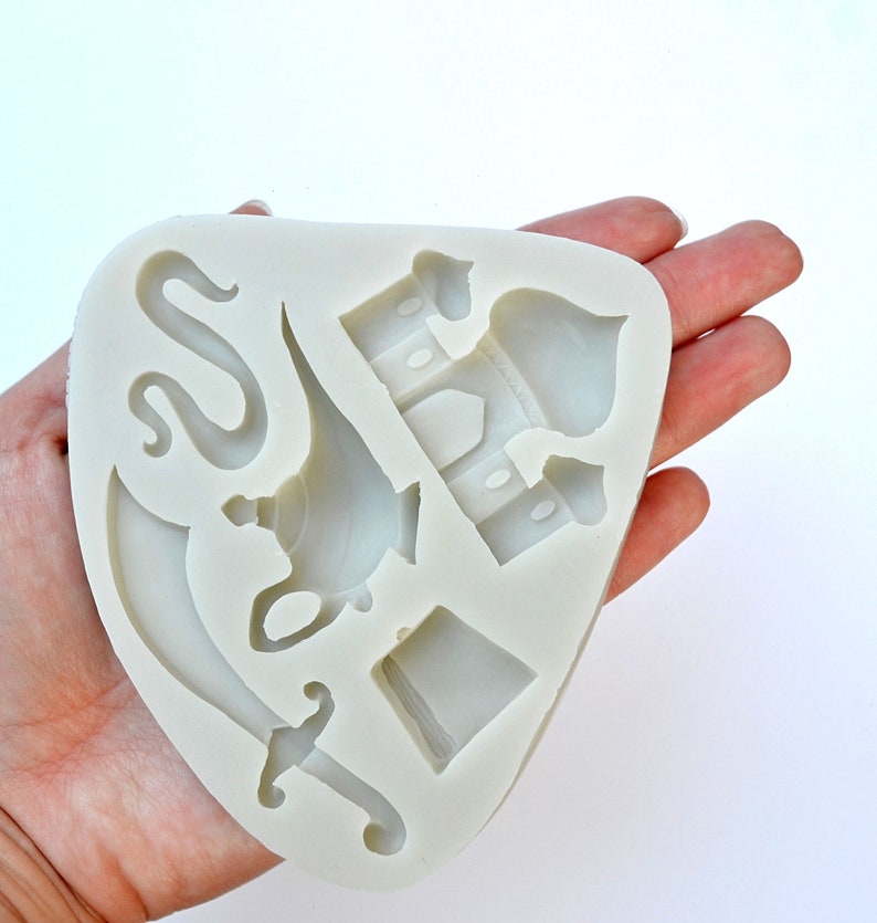 May include: A white silicone mold with five different shapes: a lamp, a sword, a snake, a hat, and a building with a dome. The mold is designed for making cake decorations.