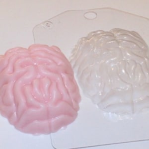 May include: A pink brain-shaped mold and a white brain-shaped mold. The molds are made of plastic and are used for making soap or candles.