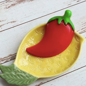 Puede incluir: Un plato de cerámica amarillo en forma de limón con hojas verdes y un chile rojo en la parte superior.