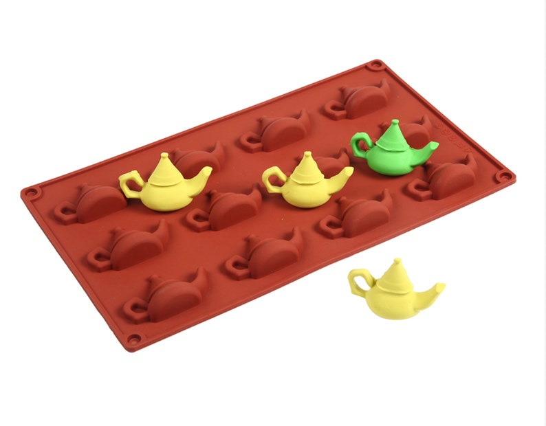 May include: A red silicone mold with 10 teapot-shaped cavities. There are three yellow and one green teapot-shaped candies in the mold.