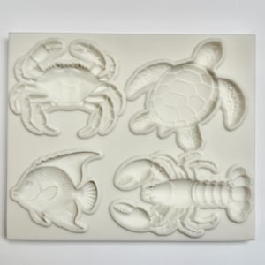 May include: A white silicone mold featuring raised designs of sea creatures. The mold includes a crab, a turtle, a fish, and a lobster. The designs are detailed and suitable for crafting or baking projects.