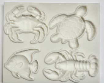 May include: A white silicone mold featuring raised designs of sea creatures. The mold includes a crab, a turtle, a fish, and a lobster. The designs are detailed and suitable for crafting or baking projects.
