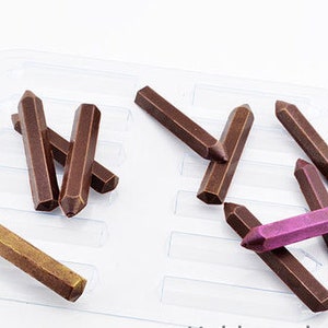 Puede incluir: Primer plano de un conjunto de 10 lápices de cera marrones y morados en una bandeja de plástico. Los lápices tienen forma de lápices y están dispuestos en varias posiciones.