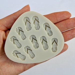 May include: A white silicone mould with eight flip-flop shapes. The flip-flops have a variety of patterns, including polka dots, stripes, and palm trees.