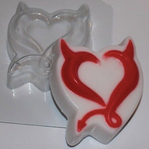 May include: A clear plastic mold of a heart with devil horns. A white soap bar with a red heart and devil horns design is in the mold.