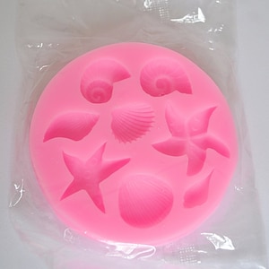 Pode incluir: Forma de silicone rosa com sete formas diferentes de conchas e estrelas do mar.