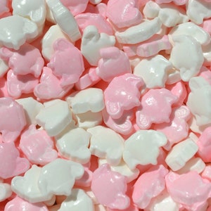 May include: Close-up of a pile of candies in the shape of baby carriages, elephants, and other shapes. The candies are white and pink, with a glossy finish. The candies are scattered across the frame.