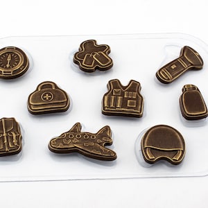 Könnte beinhalten: Eine transparente Plastikform mit neun verschiedenen Formen zum Herstellen von Schokolade. Die Formen umfassen einen Kompass, eine Erste-Hilfe-Box, einen Rucksack, eine Weste, eine Taschenlampe, eine Wasserflasche, ein Flugzeug, einen militärischen Ausweis und einen Helm.