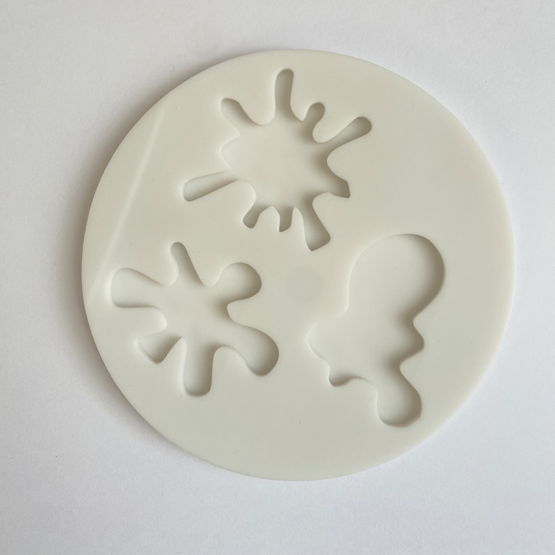 May include: White silicone mould with three shapes: two abstract splatter shapes and one abstract blob shape.